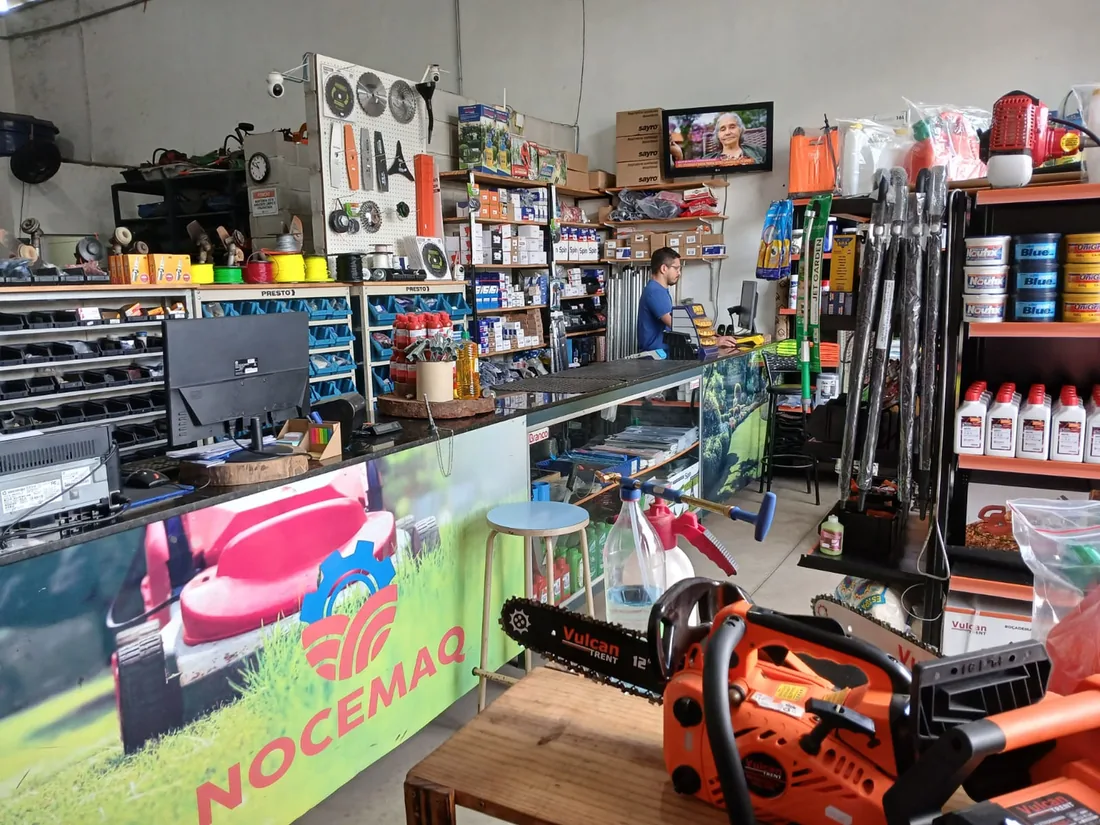 Interior da loja da Nocemaq: balcão de atendimento, prateleiras de produtos e o banner da empresa.